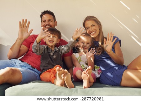 Family sitting on couch smiling and laughing together, waving at camera. Couple with kids on patio having fun outdoors in their backyard