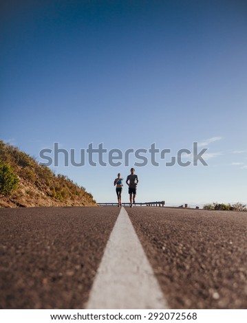 Low angle shot of two young runners training together on the road. Morning run on country road on a summer day with lots of copyspace.