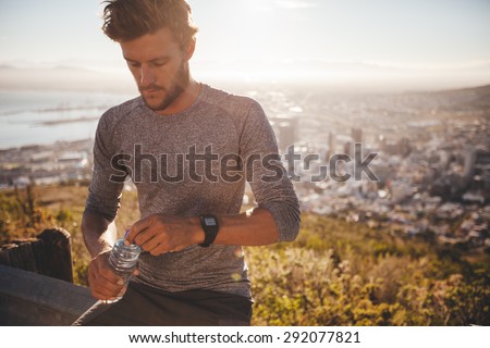 Young runner with a water bottle taking a break after hard running training outdoors. Young man relaxing after a run about to drink water.