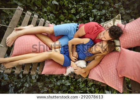 Top view of young couple lying on a garden hammock. Young man embracing his girlfriend relaxing in backyard garden.