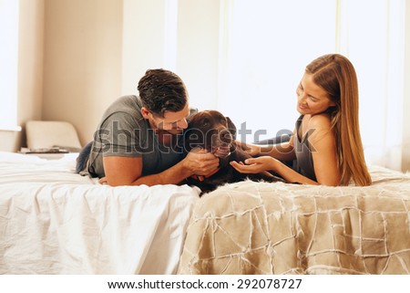 Shot of a young couple with their dog on the bed in morning. Young man and woman spending time with their pet in bedroom.