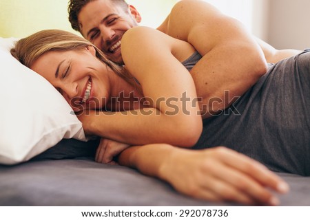 Image of cute young couple in love lying on bed. Man waking up his wife in morning.