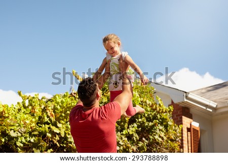 Young man lifting his daughter high in the air. Happy father and daughter playing in their backyard on a sunny day.