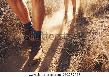 Low section shot of two young people walking on dirt trail, focus on men\'s hiking boots. Couple of hikers on country walk.