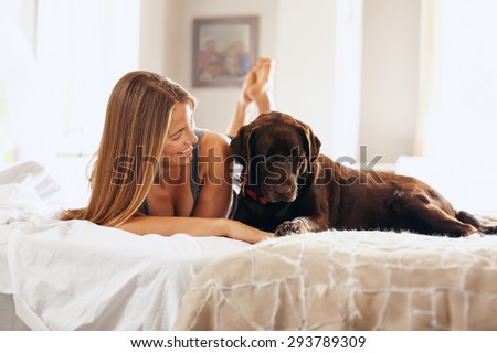 Shot of a beautiful young woman relaxing on the bed with her pet dog. Caucasian female in bedroom playing with her dog in morning.