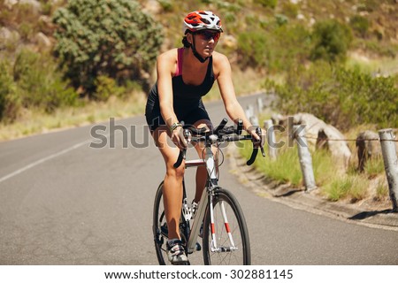 Young woman triathlon athlete cycling. Caucasian female athlete riding cycle on country road.