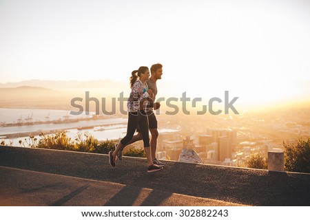 Shot of young couple running on hillside road outside the city.  Young man and woman jogging in morning with bright sunlight.