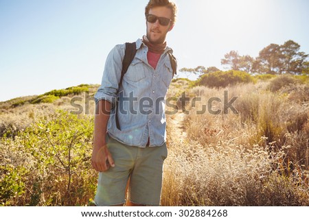 Portrait of handsome young man hiking in nature. Caucasian man walking on country trail on hot sunny day.