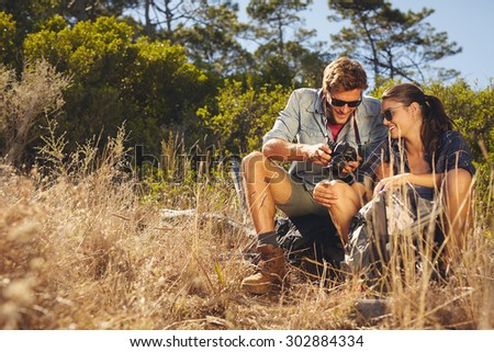 Young couple outdoors looking at photos on camera. Caucasian man and woman on hiking trip taking a break.