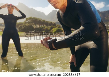 Man checking his timer. Athletes in wet suits preparing for triathlon competition.
