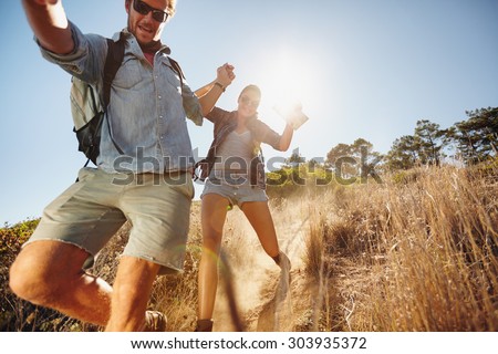 Portrait of happy young couple having fun on their hiking trip, sliding down the mountain trail. Caucasian hiker couple enjoying themselves on summer vacation.