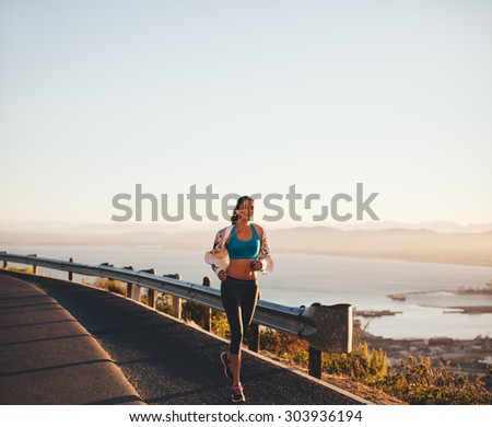 Outdoor shot of a young woman on her morning run. Female athlete running on country road.