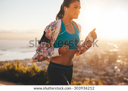 Shot of confident young runner in sportswear on morning run. Woman jogging in morning with bright sunlight.
