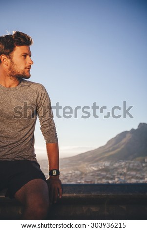 Fitness male athlete resting after outdoors training. Young man relaxing after morning run looking away at copy space.