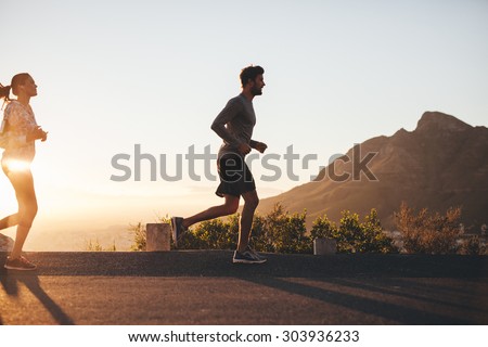 Outdoor shot of young couple on morning run. Young man and woman jogging on road outside during sunrise.