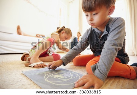 Little boy drawing and coloring while sitting on floor in living room. Children on floor painting with parents sitting on sofa in background.