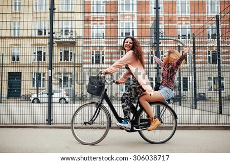Portrait of two happy young women enjoying bike ride on city street. Female friends riding on one bicycle.