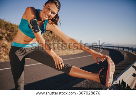 Female athlete stretching her legs outdoor before running. Fit young woman warming up for a run on country road.