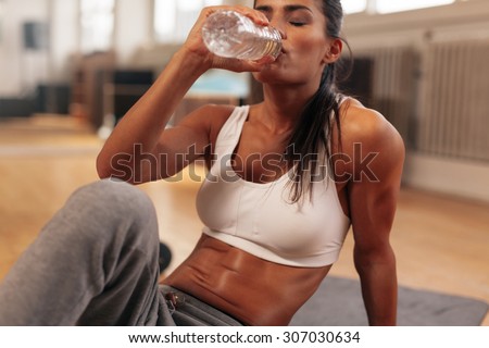 Fitness woman drinking water from bottle. Muscular young female at gym taking a break from workout.