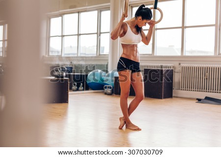 Fit woman using gymnast rings at the gym. Muscular young female athlete exercising with rings.
