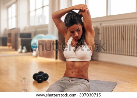 Fitness woman doing stretching exercise. Young woman stretching her arms while sitting on exercise mat at gym.
