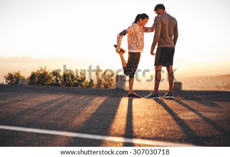 Outdoor shot of fit young joggers stretching before a run together in morning. Young man standing and woman stretching her legs at sunrise.