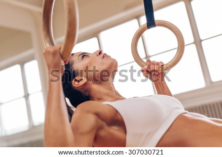 Close up shot of strong young woman doing pull-ups with gymnastic rings. Fitness female athlete exercising at gym.