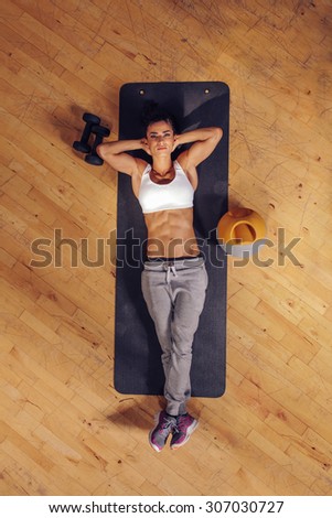 Top view of woman relaxing on yoga mat. Fitness female lying on exercise mat with her hands behind head and looking at camera at gym.