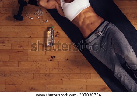Cropped shot of woman relaxing after exercise session with a water bottle on floor. Top view of young woman lying on exercise mat in gym.