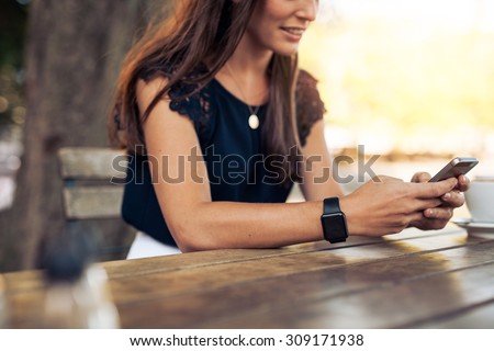 Woman typing text message on smart phone in a cafe. Cropped image of young woman sitting at a table with a coffee using mobile phone.