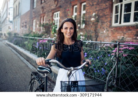 Beautiful woman with a cycle walking down the city road. Caucasian female smiling and looking at camera.