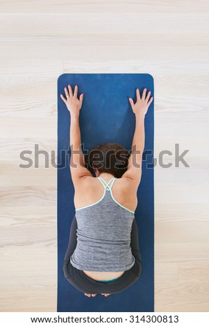 Top view of woman curls up and stretches forward, performing a yoga. Fitness female on exercise mat over light hardwood floors at health club. Woman practicing yoga at gym. Balasana pose.