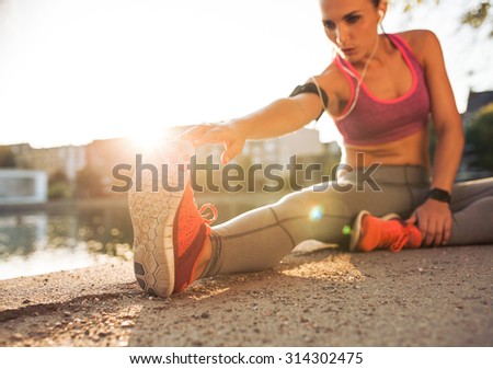 Young woman runner stretching legs before doing her summer workout. Sportswoman warming up before outdoor workout.