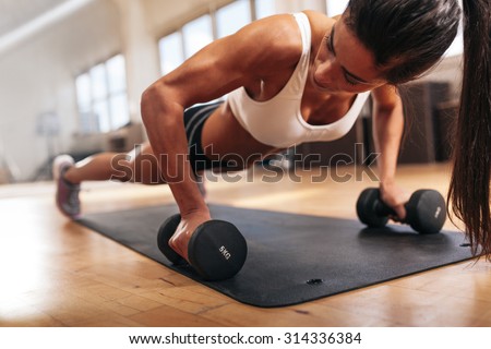 Gym woman doing push-up exercise with dumbbell. Strong female doing crossfit workout.