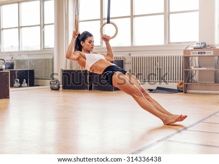 Young fit woman doing pull-ups on gymnastic rings. Muscular young female athlete exercising with rings at gym.