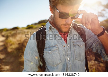 Close up shot of young man on country hike. Caucasian male model hiking wearing sunglasses with sun flare.
