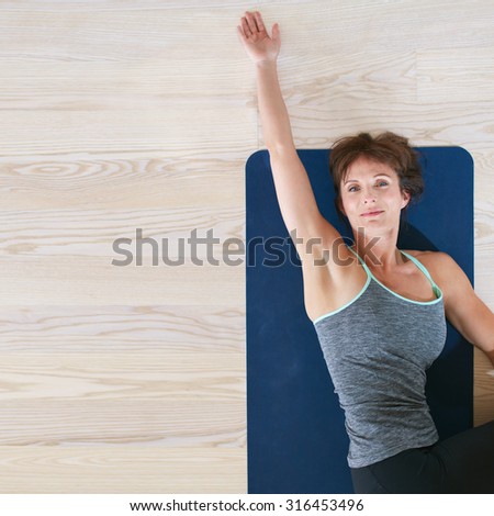 Top view of woman lying and stretching on exercise mat. Female on floor twisting her body and stretching her one hand.