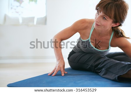 Image of woman bending forward doing yoga . Fitness woman practicing yoga on exercise mat at gym looking away.
