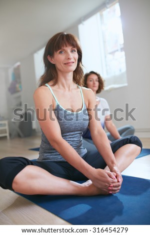 Portrait of female fitness trainer sitting on floor in Baddha konasana yoga pose. Women in yoga class sitting in butterfly pose.