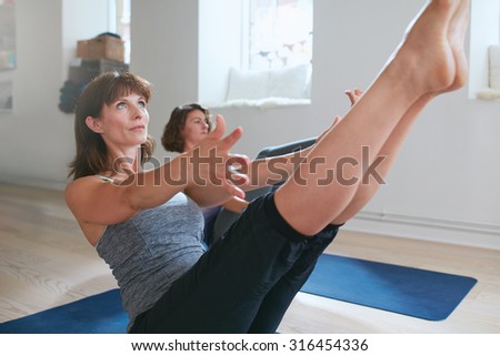 Women practicing stretching and yoga workout exercise together in a health club gym training class session. Two women practicing yoga, bending in boat pose. Performing Navasana in yoga class.