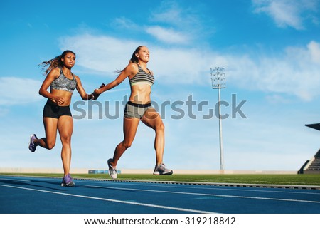 Young woman running a relay race and giving relay baton to her teammate. Female runner passing the relay baton during race.