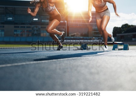 Sprinters starts out of the blocks on athletics racetrack with bright sunlight. Low section shot of female athletes starting a race in stadium with sunflare.