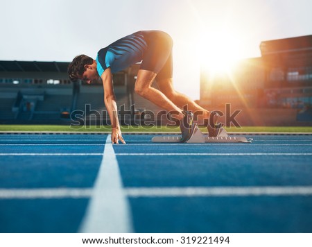 Male athlete on starting position at athletics running track. Runner practicing his sprint start in athletics stadium racetrack.