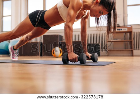 Strong young woman doing push ups exercise with dumbbells on yoga mat. Fitness model doing intense training in the gym.