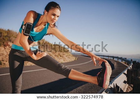 Determined young woman warming up before a run. Female athlete stretching her leg on road guardrail in morning.
