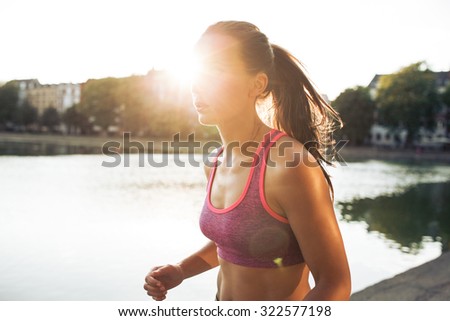 Outdoor shot of determined young woman out for a run in city park. Sportswoman jogging on a summer day with sun flare.