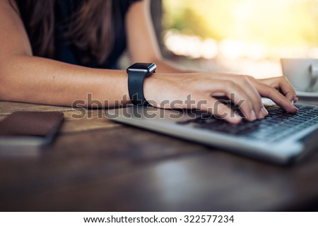 Hands of woman wearing smartwatch on the keyboard of her laptop computer. Female working on laptop in a cafe.