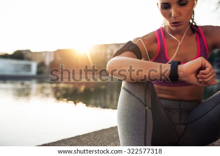 Beautiful young woman sitting outdoors using a smartwatch to monitor her progress. Caucasian female runner resting and checking her performance on fitness smart watch device.