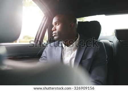 Young african businessman traveling to work in the luxury car on the back seat looking outside the window.