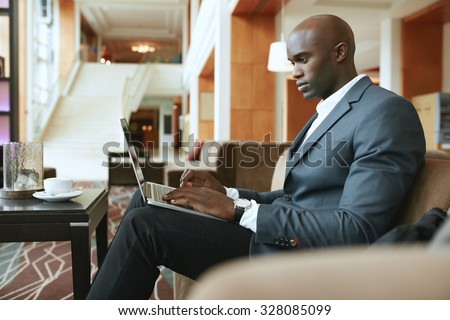 Image of busy young businessman working on laptop. African businessman sitting in hotel lobby waiting for someone.